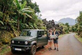 Couple en road trip à La Réunion debout près d'un SUV compact sur une route sinueuse entourée de végétation tropicale et de roches volcaniques