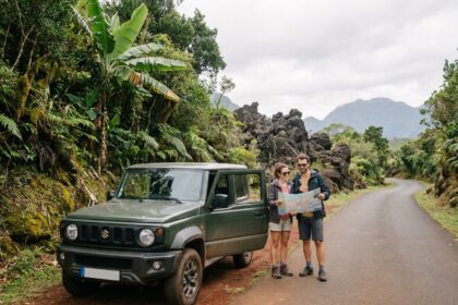 Couple en road trip à La Réunion debout près d'un SUV compact sur une route sinueuse entourée de végétation tropicale et de roches volcaniques