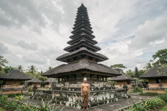 Vue en contre-plongée des tours meru du temple Taman Ayun à Bali, avec un homme en tenue traditionnelle balinaise au premier plan